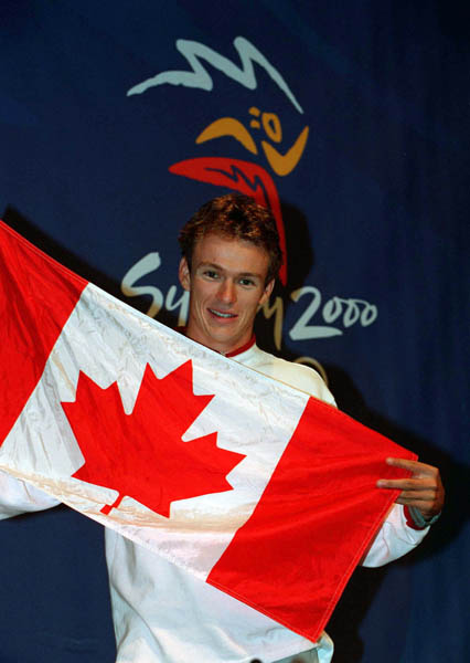 Canada's Simon Whitfield, gold medallist of the men's triathlon, holds the Canadian flag at the 2000 Sydney Olympic Games. (CP Photo/ COA)