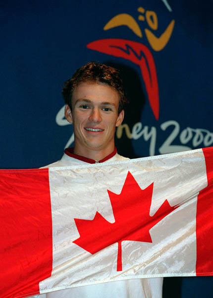 Canada's Simon Whitfield, gold medallist of the men's triathlon, holds the Canadian flag at the 2000 Sydney Olympic Games. (CP Photo/ COA)