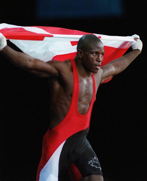 Canada's Daniel Igali waves the flag in triumph after having won the gold medal for wrestling at the 2000 Sydney Olympic Games. (CP Photo/ COA)