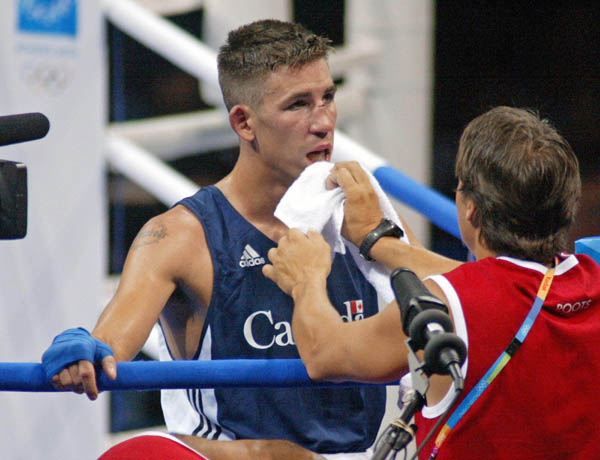 Adam Trupish (left) of Windsor, Ont. has an injury tended to by a trainer during his bout with Ruslan Khairov of Azerbiajan at the Athens Olympics Sunday, August 15, 2004. Trupish lost the bout due to the cut. (CP PHOTO/COC-Mike Ridewood)