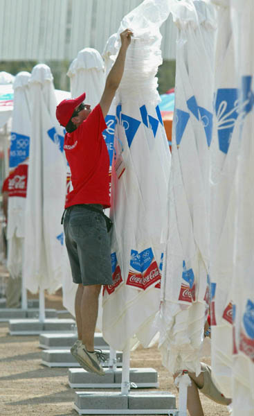 A worker pulls plastic off an umbrella in a food court at the Athens Olympic Sports Complex in Athens, Saturday, Aug. 7, 2004. Opening ceremonies take place next Friday.  (CP PHOTO/ho, COC - Mike Ridewood)