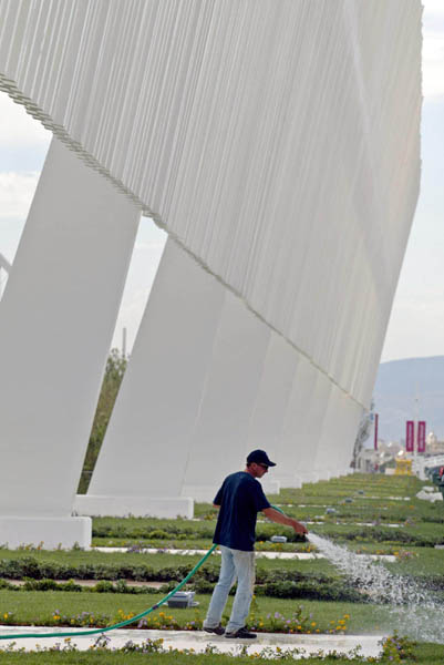 A worker waters the fresh landscaping in front of the Aquatic Centre at the Athens Olympic Sports Complex in Athens, Saturday, Aug. 7, 2004. Opening ceremonies take place next Friday.  (CP PHOTO/ho, COC - Mike Ridewood)