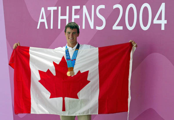 Canada's Adam van Koeverden of Toronto poses with his gold and bronze medals and a Canadian flag after being named the flag bearer for the closing ceremonies at the Athens Olympics Sunday, August 29, 2004.(CP PHOTO/COC-Mike Ridewood)