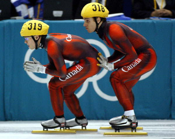 Canadian short track speed skater Franois-Louis Tremblay (318) pushes off teammate Mathieu Turcotte (319) during the 5,000 metre heat in Salt Lake City at the 2002 Olympic Winter Games. (CP Photo/COA/Andre Forget).