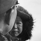 Photograph of an Inuit man and a boy being pulled on a dog sled, unknown location, Nunavut, 1962